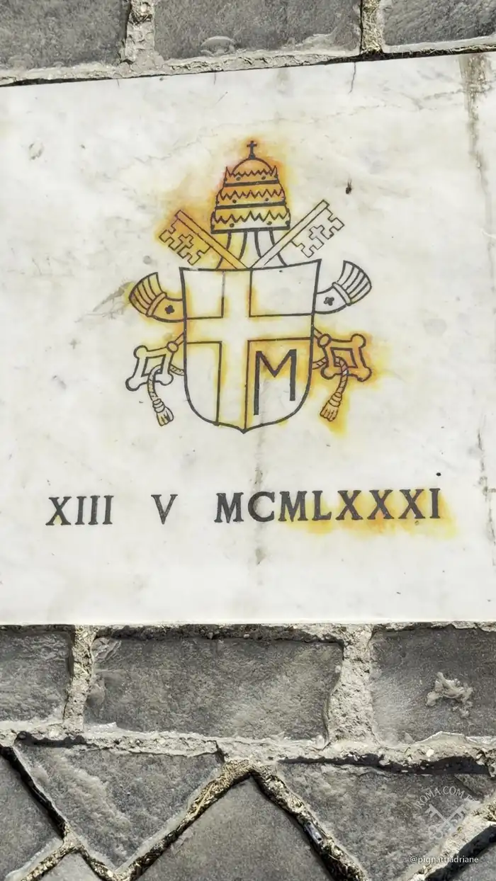 A placa de mármore no calçamento, com o brasão de João Paulo II e a data XIII V MCMLXXXI, 13 de maio de 1981.